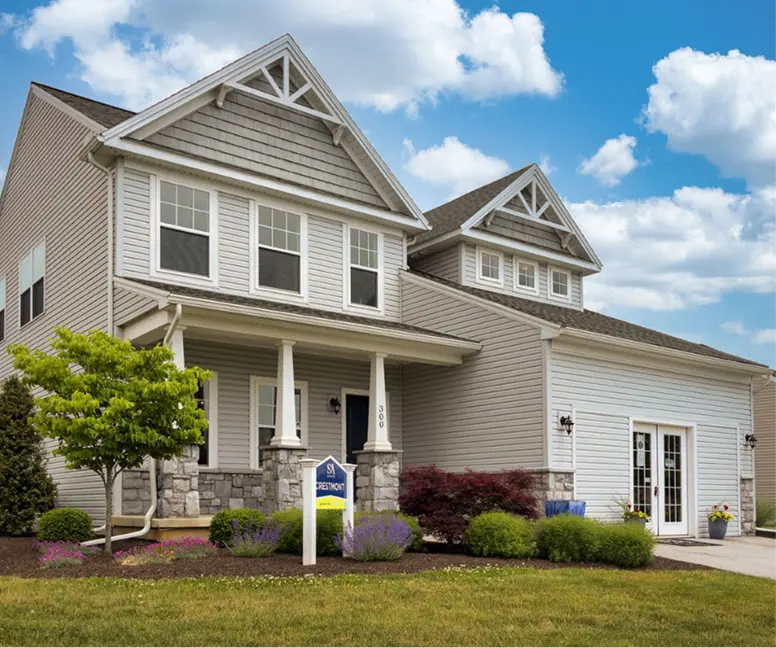 Two-Story Crestmont S&A model home with light siding, stone accents, covered front porch, attached garage, and landscaped yard. 