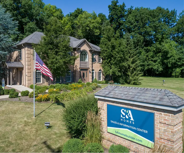 S&A Homes sales office with brick building, monument sign, American flag, and tree-lined setting.