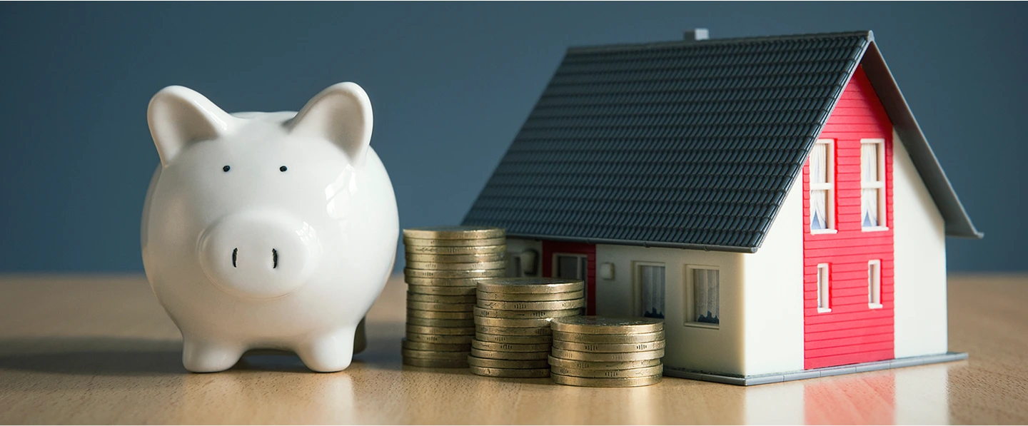 Piggy bank with coins next to a toy house